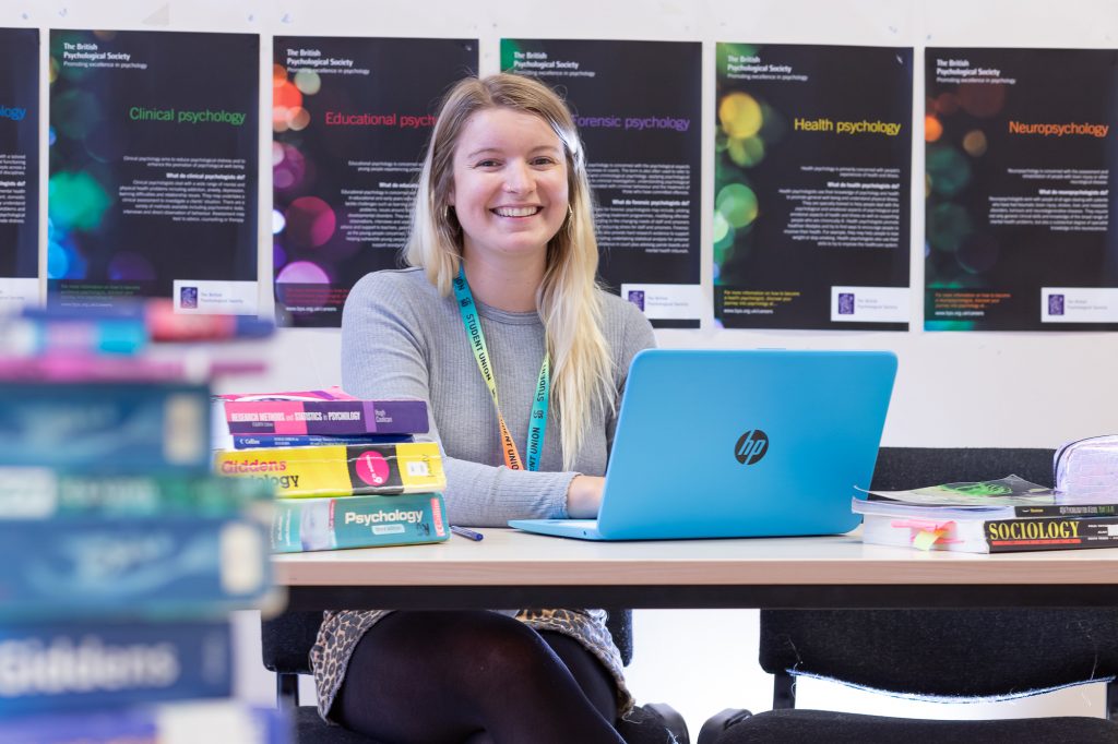 Student smiling while sitting at desk with laptop and books