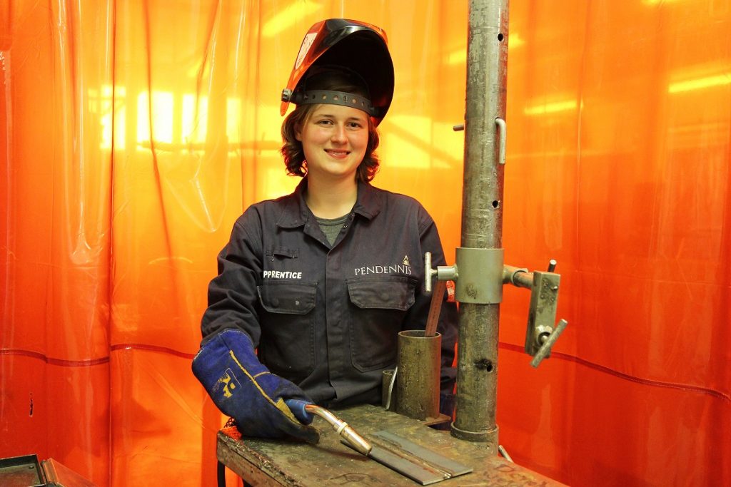 Engineering student standing in front of machine, wearing protective gear 