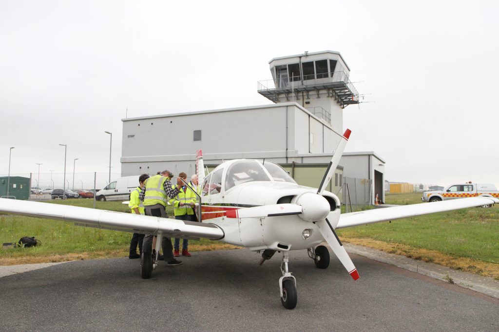 Three men standing next to a small airplane at Newquay airport