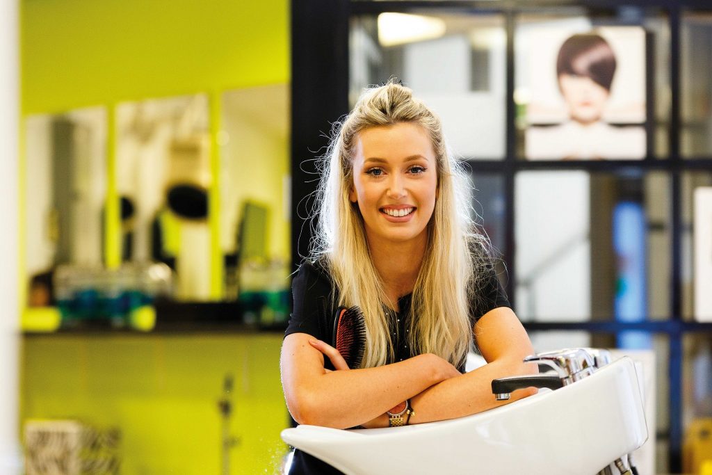 Hair student smiling and standing next to basin at the salon