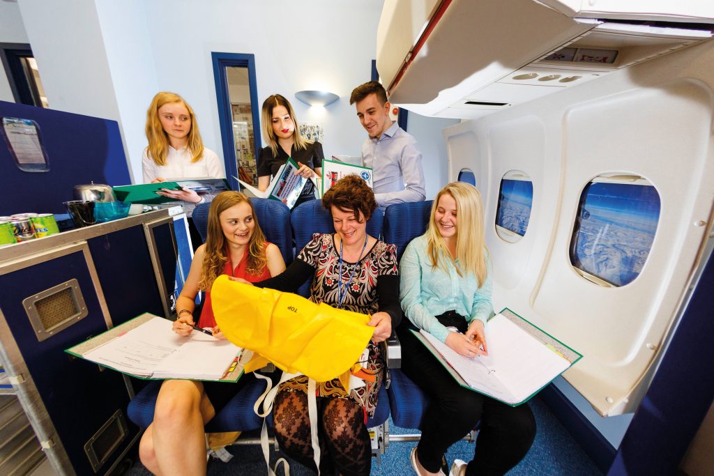 Travel and tourism students and teacher sitting on airplane simulator in classroom