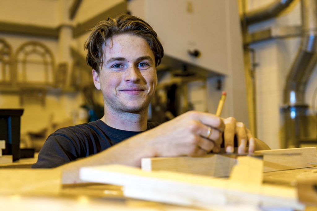 Man smiling while standing in front of wood pieces