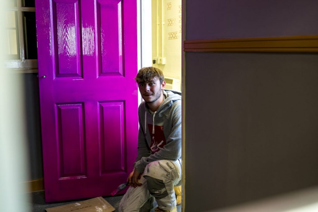 Painting and Decorating student sitting next to newly painted purple door