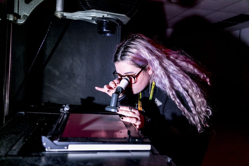 Photography student examining photo with binoculars in lab