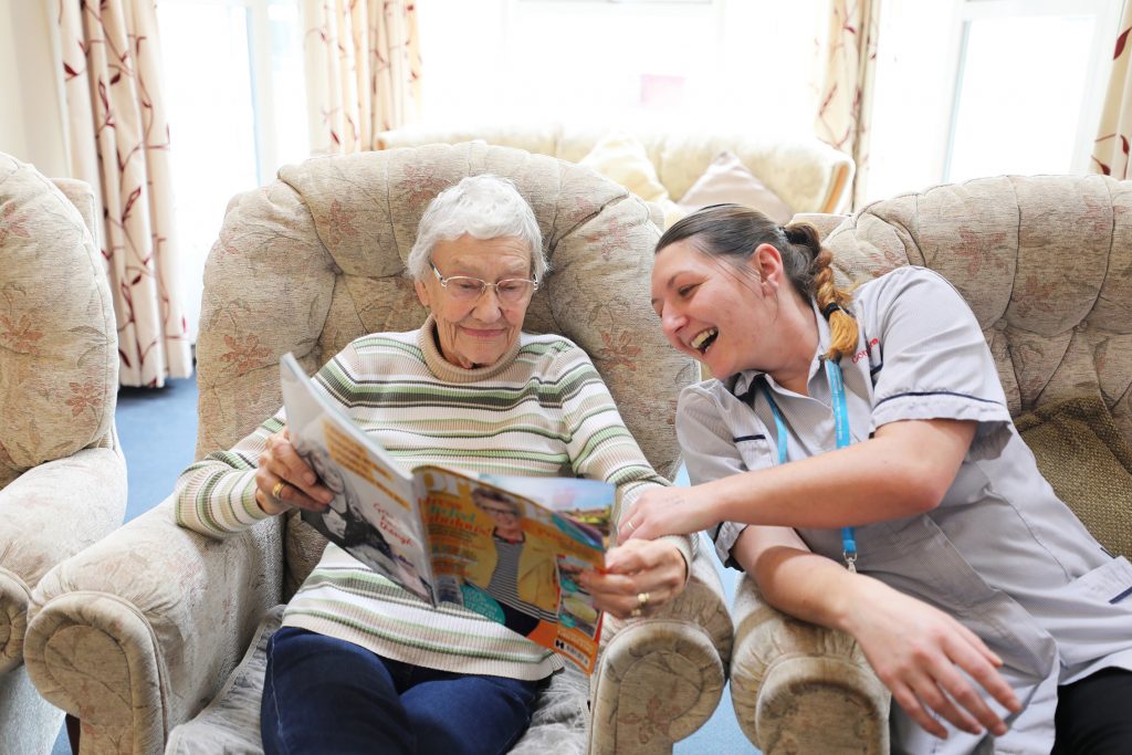 Female caregiver and elderly woman reading together